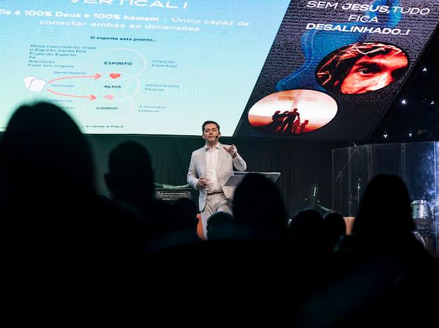 Tela de palco com a frase Sem Jesus tudo fica desalinhado, enquanto Gustavo Coelho gesticula ao falar